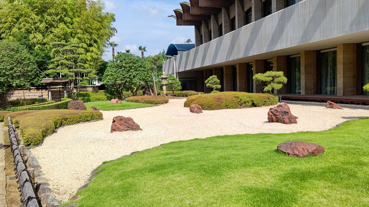 白い砂を敷いた庭に石と刈り込んだ植え込みが置かれ、奥にホテルの建物が建つ